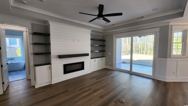 unfurnished living room featuring ceiling fan, a large fireplace, a tray ceiling, and dark hardwood / wood-style floors