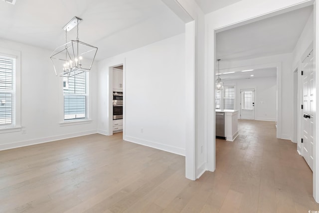 unfurnished dining area featuring baseboards, a chandelier, and light wood-style floors