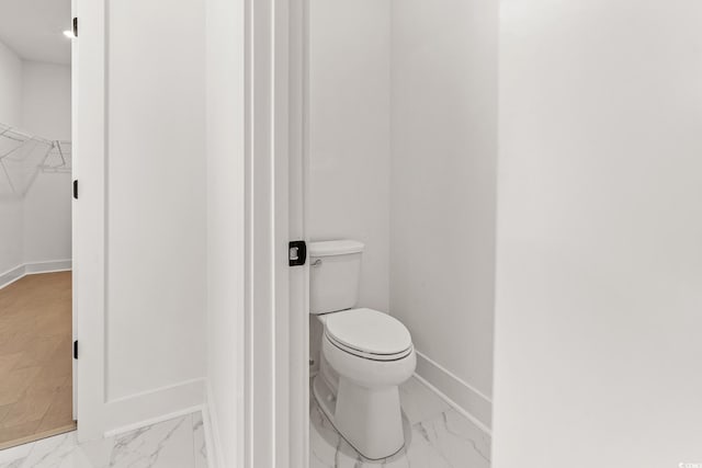 bathroom featuring a walk in closet, marble finish floor, toilet, and baseboards