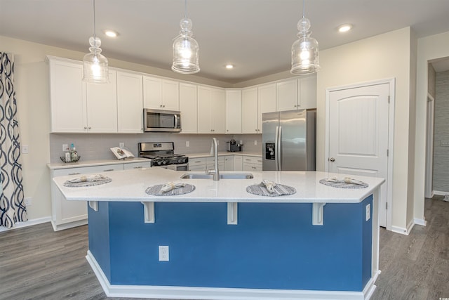 kitchen with sink, hanging light fixtures, a kitchen island with sink, appliances with stainless steel finishes, and hardwood / wood-style flooring