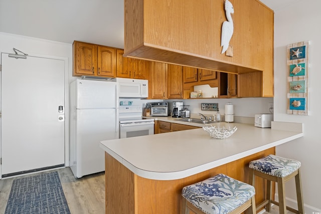 kitchen with kitchen peninsula, white appliances, sink, light hardwood / wood-style flooring, and a breakfast bar area