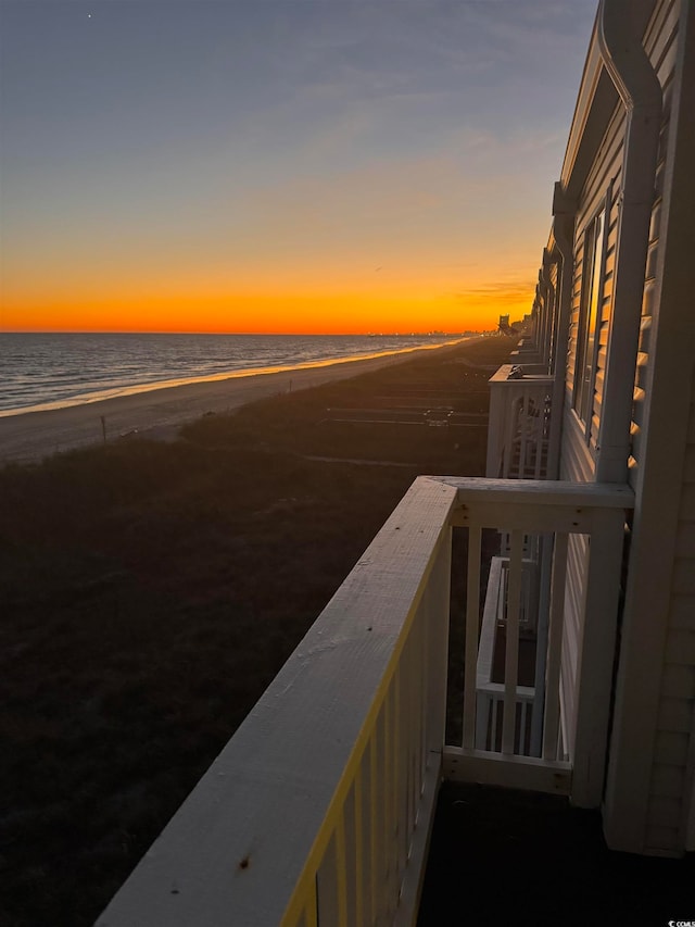 balcony at dusk featuring a water view and a beach view