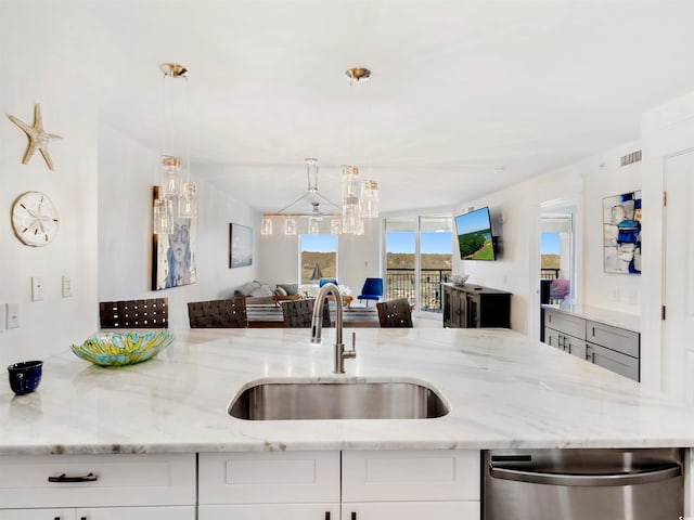 kitchen featuring light stone countertops, sink, white cabinets, and pendant lighting