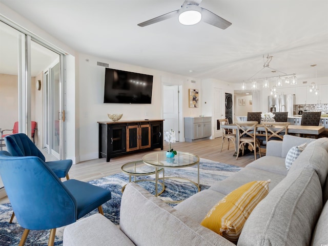 living room with light wood-type flooring, stacked washer and dryer, ceiling fan, and rail lighting