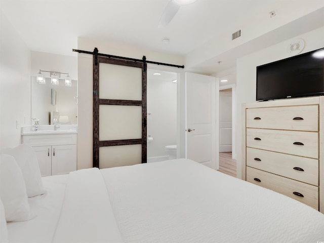 bedroom with ensuite bathroom, a barn door, light hardwood / wood-style floors, and ceiling fan