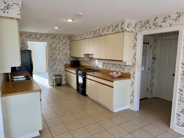 kitchen with light tile patterned floors, a sink, black appliances, and wallpapered walls