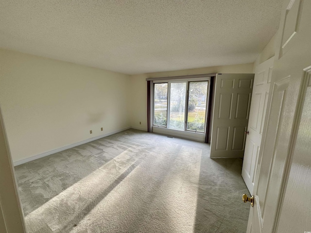 unfurnished room featuring light carpet, a textured ceiling, and baseboards