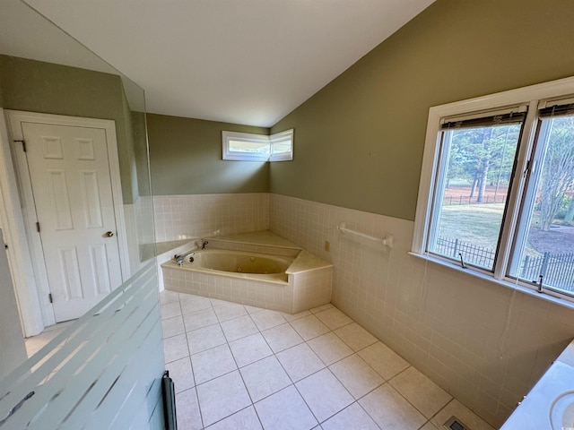 bathroom with a wainscoted wall, tile walls, lofted ceiling, tile patterned flooring, and a jetted tub