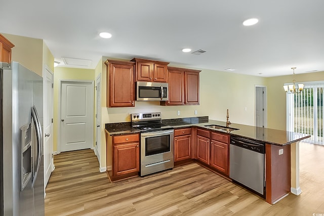 kitchen with kitchen peninsula, appliances with stainless steel finishes, a chandelier, and light hardwood / wood-style flooring