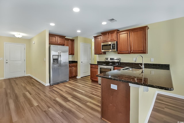 kitchen featuring kitchen peninsula, appliances with stainless steel finishes, dark stone counters, sink, and light hardwood / wood-style flooring