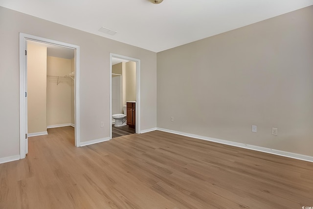 unfurnished bedroom with light hardwood / wood-style flooring, a spacious closet, a closet, and ensuite bathroom