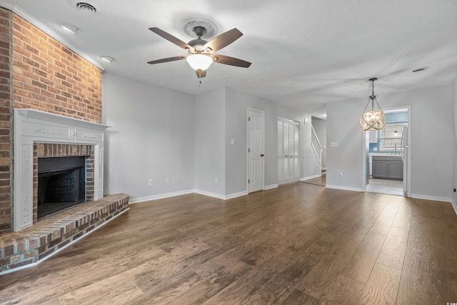 unfurnished living room with ceiling fan with notable chandelier, wood-type flooring, and a brick fireplace