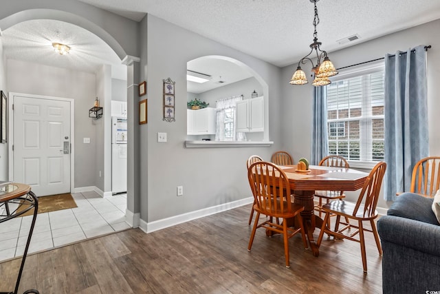 dining space with a textured ceiling, light wood-type flooring, and a notable chandelier