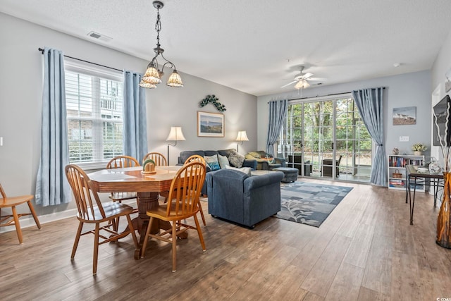 dining space with wood-type flooring, ceiling fan with notable chandelier, a textured ceiling, and plenty of natural light