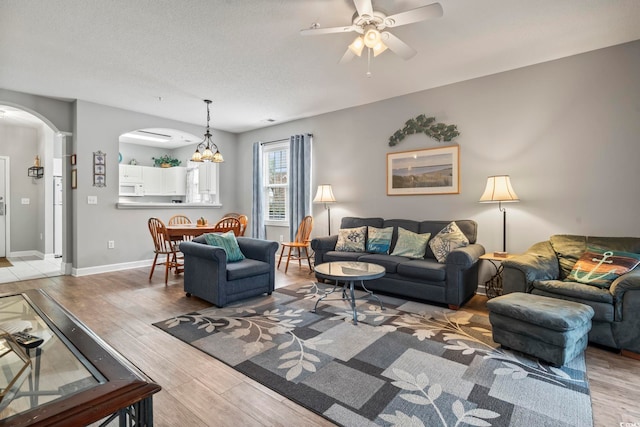 living room with ceiling fan with notable chandelier, a textured ceiling, and light hardwood / wood-style flooring