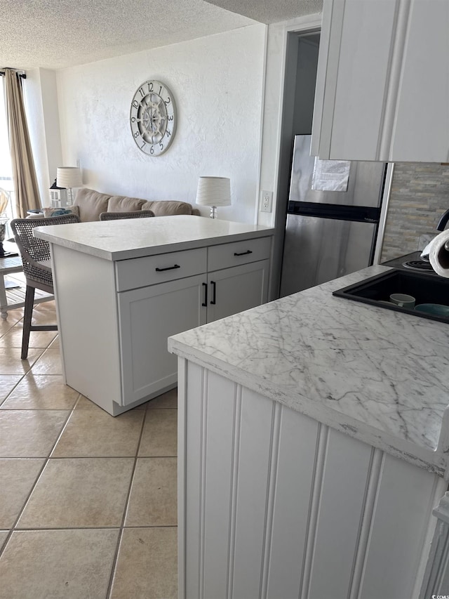 kitchen featuring white cabinetry, a textured ceiling, light tile patterned flooring, kitchen peninsula, and stainless steel fridge