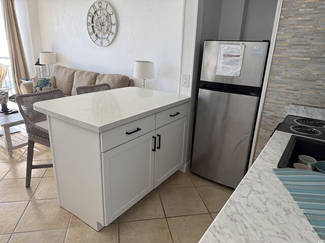 kitchen featuring a kitchen breakfast bar, light tile patterned flooring, white cabinetry, and stainless steel refrigerator