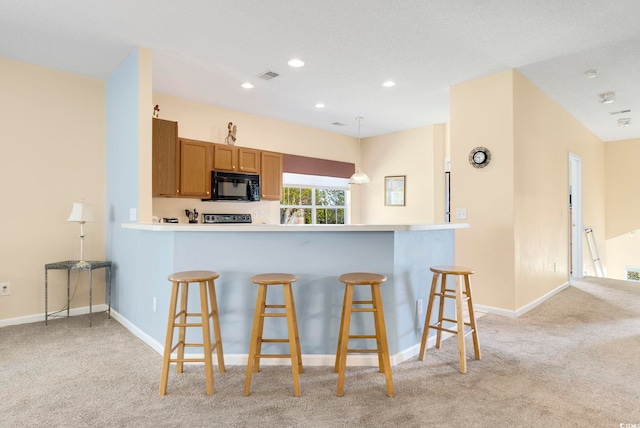 kitchen featuring black microwave, a peninsula, hanging light fixtures, light countertops, and brown cabinets