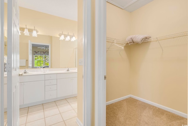 bathroom with a walk in closet, double vanity, a sink, tile patterned flooring, and baseboards