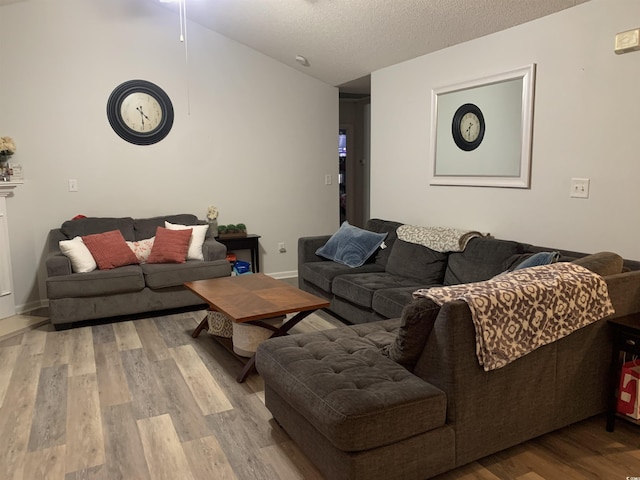 living room with a textured ceiling, light wood-type flooring, and vaulted ceiling