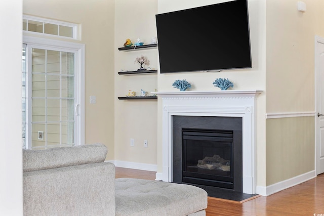 living area with a glass covered fireplace, baseboards, and wood finished floors