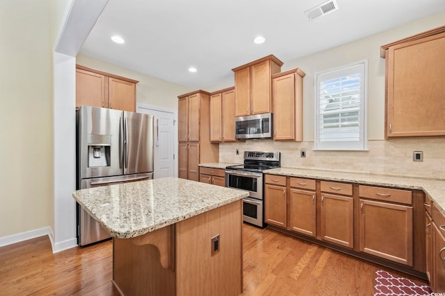 kitchen with appliances with stainless steel finishes, a center island, visible vents, and light stone countertops