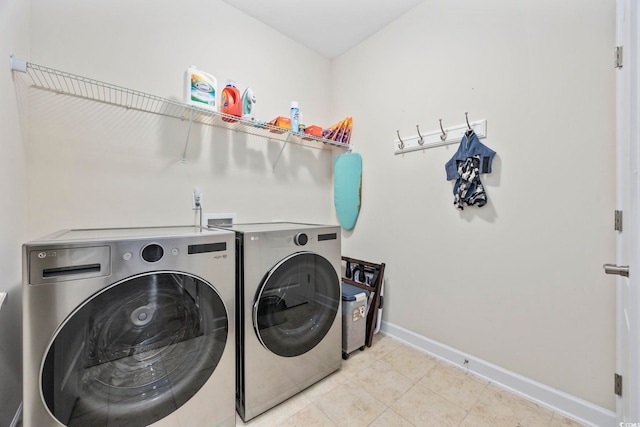 washroom featuring laundry area, baseboards, separate washer and dryer, and light tile patterned flooring