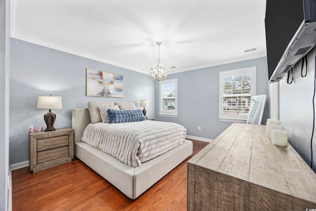 bedroom featuring visible vents, baseboards, ornamental molding, wood finished floors, and an inviting chandelier