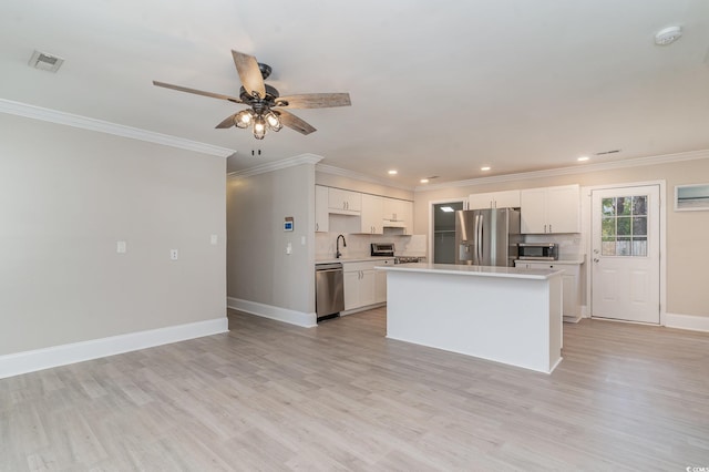 kitchen featuring appliances with stainless steel finishes, white cabinetry, sink, backsplash, and a center island