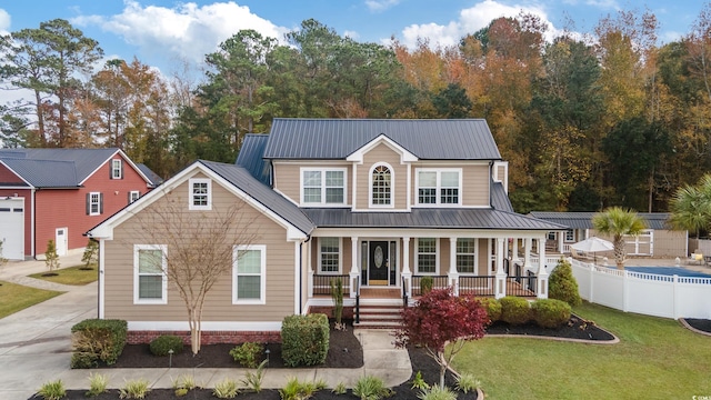 view of front of property featuring metal roof, a porch, fence, driveway, and a front lawn