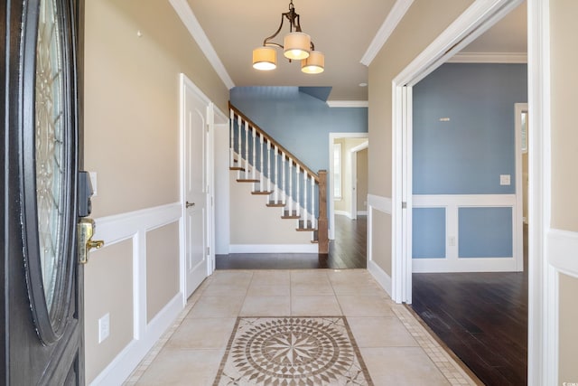 foyer with light tile patterned floors, a decorative wall, stairs, and crown molding