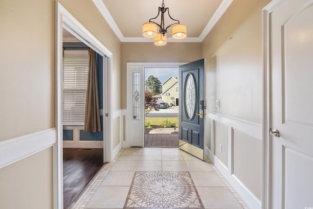 entrance foyer featuring light tile patterned floors, a wainscoted wall, crown molding, a decorative wall, and a notable chandelier