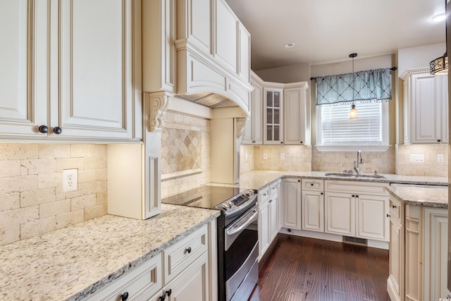 kitchen with light stone counters, glass insert cabinets, hanging light fixtures, stainless steel electric stove, and a sink