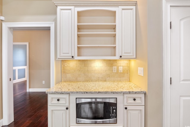 kitchen with open shelves, stainless steel microwave, backsplash, and light stone countertops