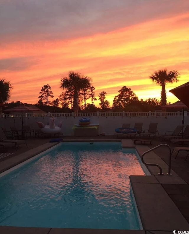 pool at dusk with a fenced in pool, a fenced backyard, and a patio