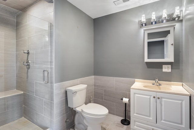 bathroom featuring tile walls, toilet, wainscoting, a shower stall, and vanity