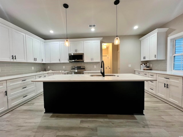 kitchen with white cabinets, stainless steel appliances, a center island with sink, and sink