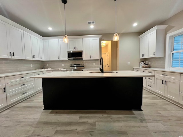 kitchen featuring hanging light fixtures, sink, a kitchen island with sink, and appliances with stainless steel finishes