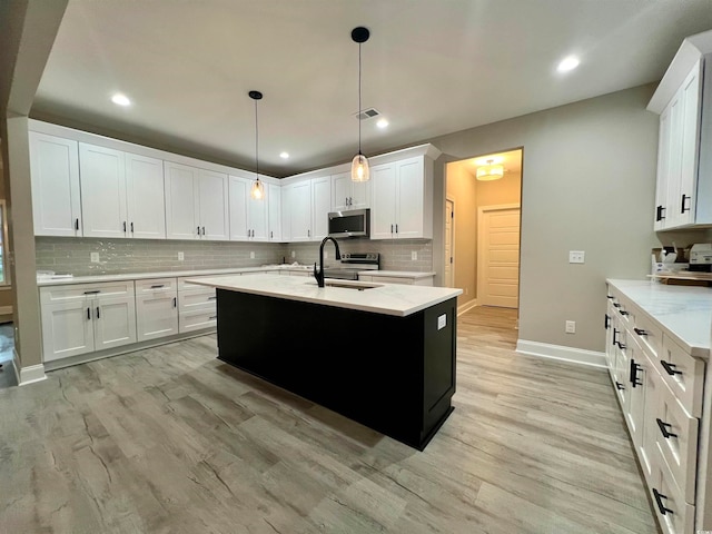 kitchen featuring white cabinets, sink, hanging light fixtures, light hardwood / wood-style flooring, and an island with sink