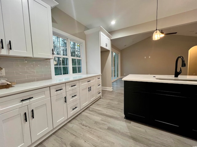 kitchen featuring lofted ceiling, white cabinets, sink, light hardwood / wood-style flooring, and tasteful backsplash