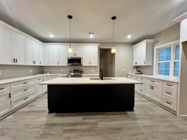 kitchen featuring decorative light fixtures, sink, stainless steel appliances, and an island with sink