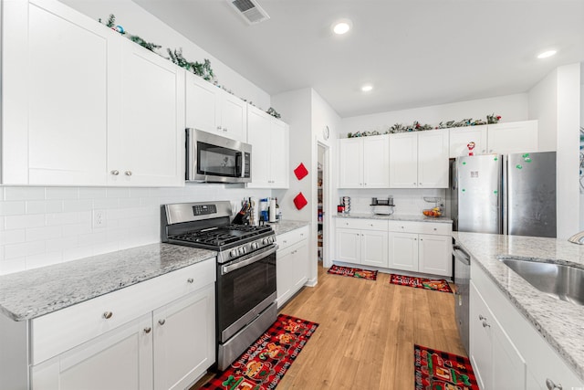 kitchen with white cabinets, appliances with stainless steel finishes, light hardwood / wood-style floors, and light stone counters