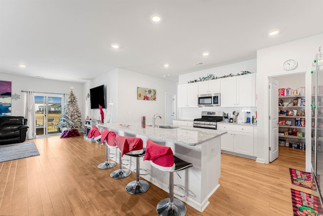 kitchen with stainless steel appliances, a kitchen island with sink, sink, light hardwood / wood-style flooring, and white cabinetry