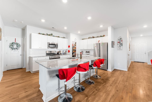 kitchen with appliances with stainless steel finishes, sink, a center island with sink, light hardwood / wood-style flooring, and white cabinets