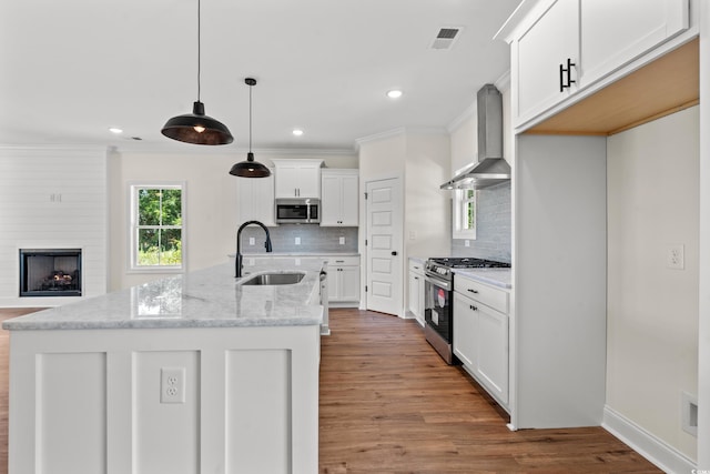 kitchen with wall chimney range hood, sink, light stone countertops, appliances with stainless steel finishes, and decorative light fixtures