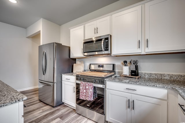 kitchen featuring white cabinets, appliances with stainless steel finishes, light hardwood / wood-style flooring, and light stone counters