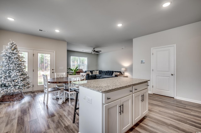 kitchen featuring light stone countertops, ceiling fan, a center island, light hardwood / wood-style floors, and white cabinets