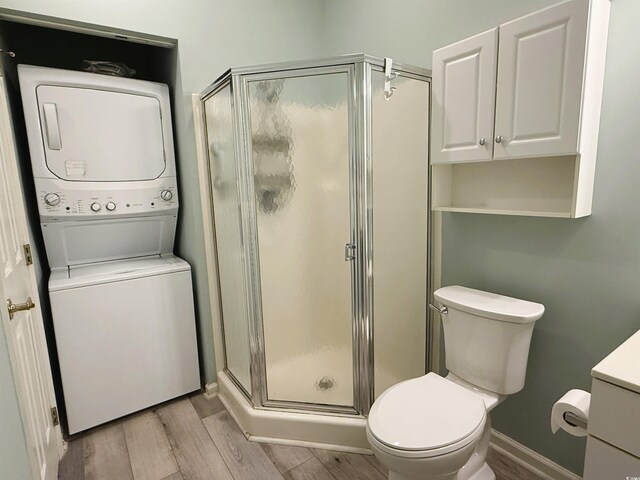 bathroom featuring an enclosed shower, vanity, wood-type flooring, stacked washer and dryer, and toilet