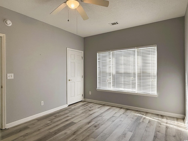 empty room featuring a textured ceiling, light wood-type flooring, and ceiling fan