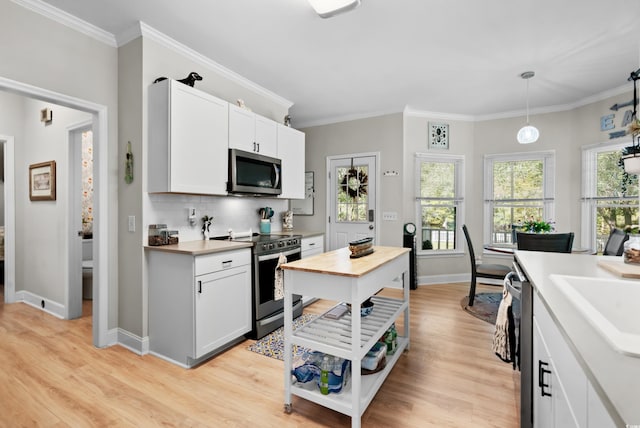 kitchen featuring white cabinets, crown molding, hanging light fixtures, light wood-type flooring, and appliances with stainless steel finishes